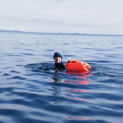 A person in a cosy hat in still blue sea with a float bag