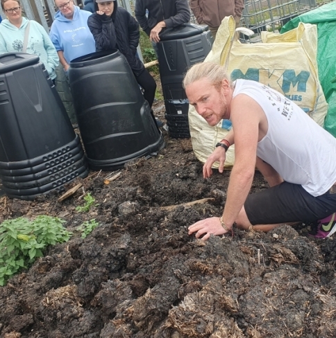 A man in a sleeveless white shirt sits on a manure pile, explaining about biodiversity