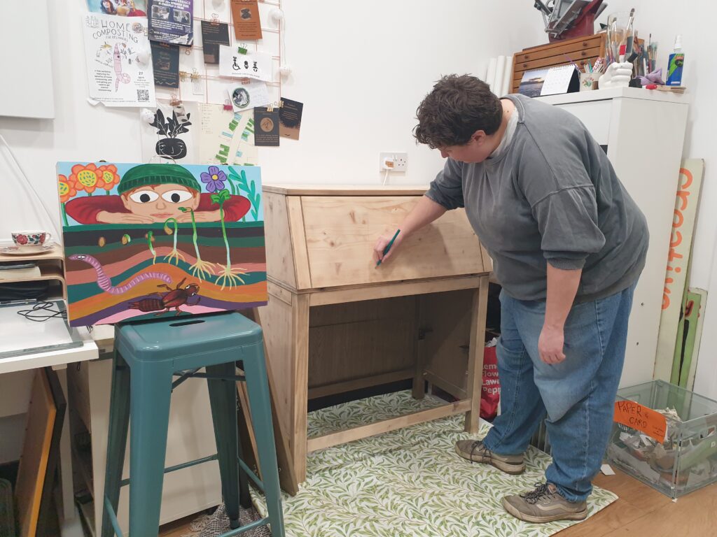 An artist sketching out a painting on  a wooden cabinet.