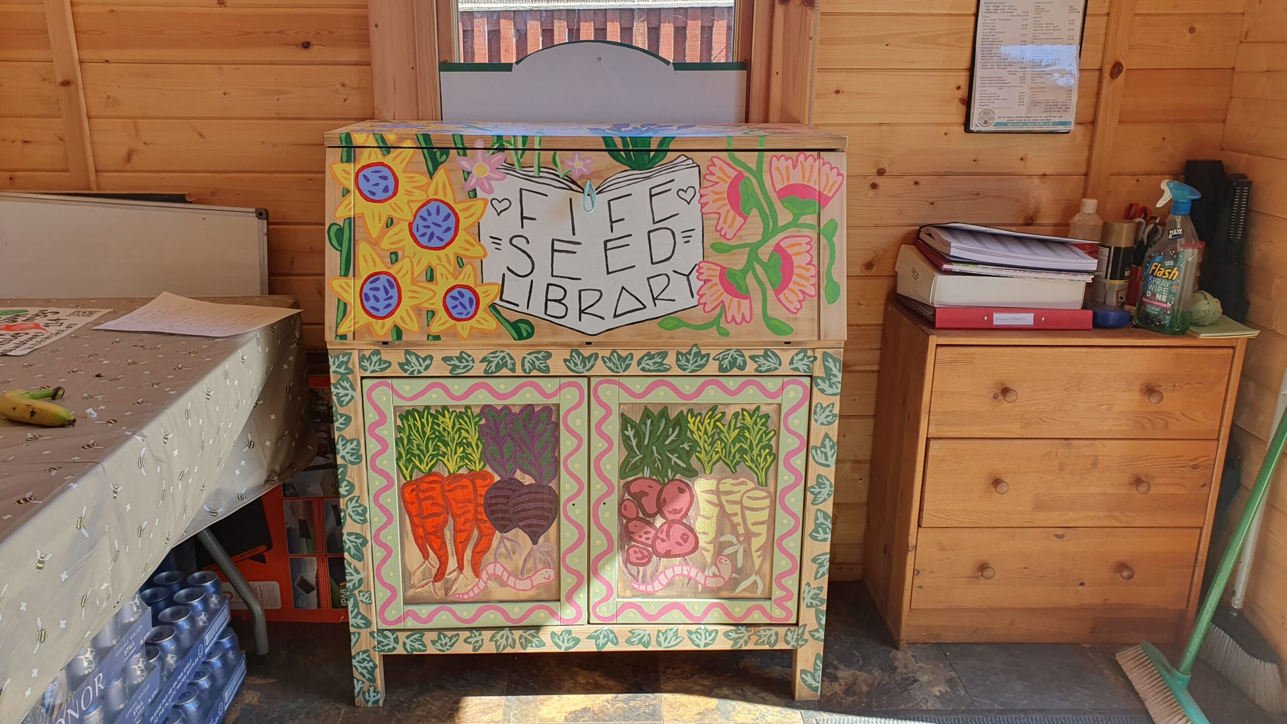 Cabinet painted with bright vegetables and flowers against a wooden wall