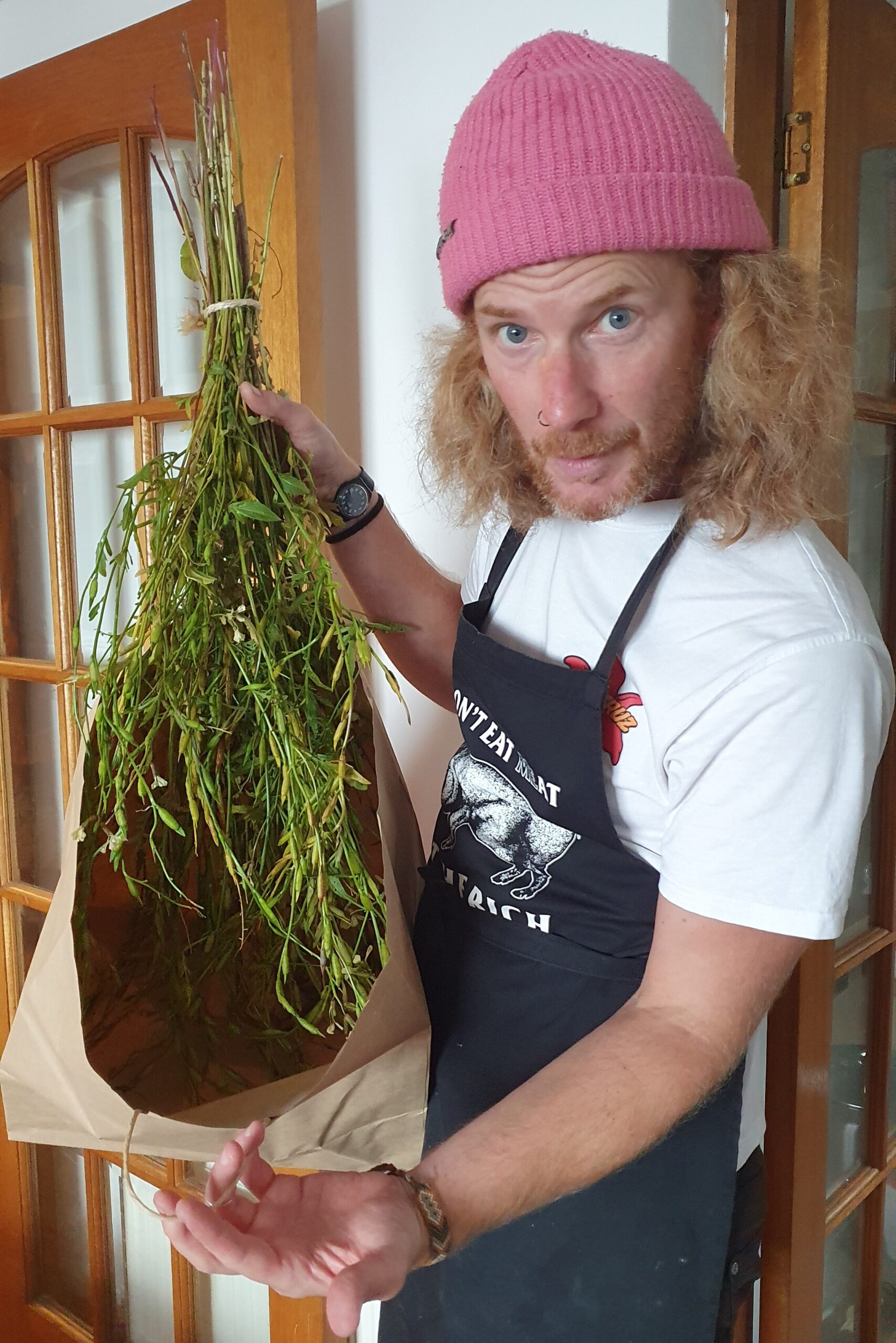 A white man in a pink hat holding a bouquet of seeding rocket